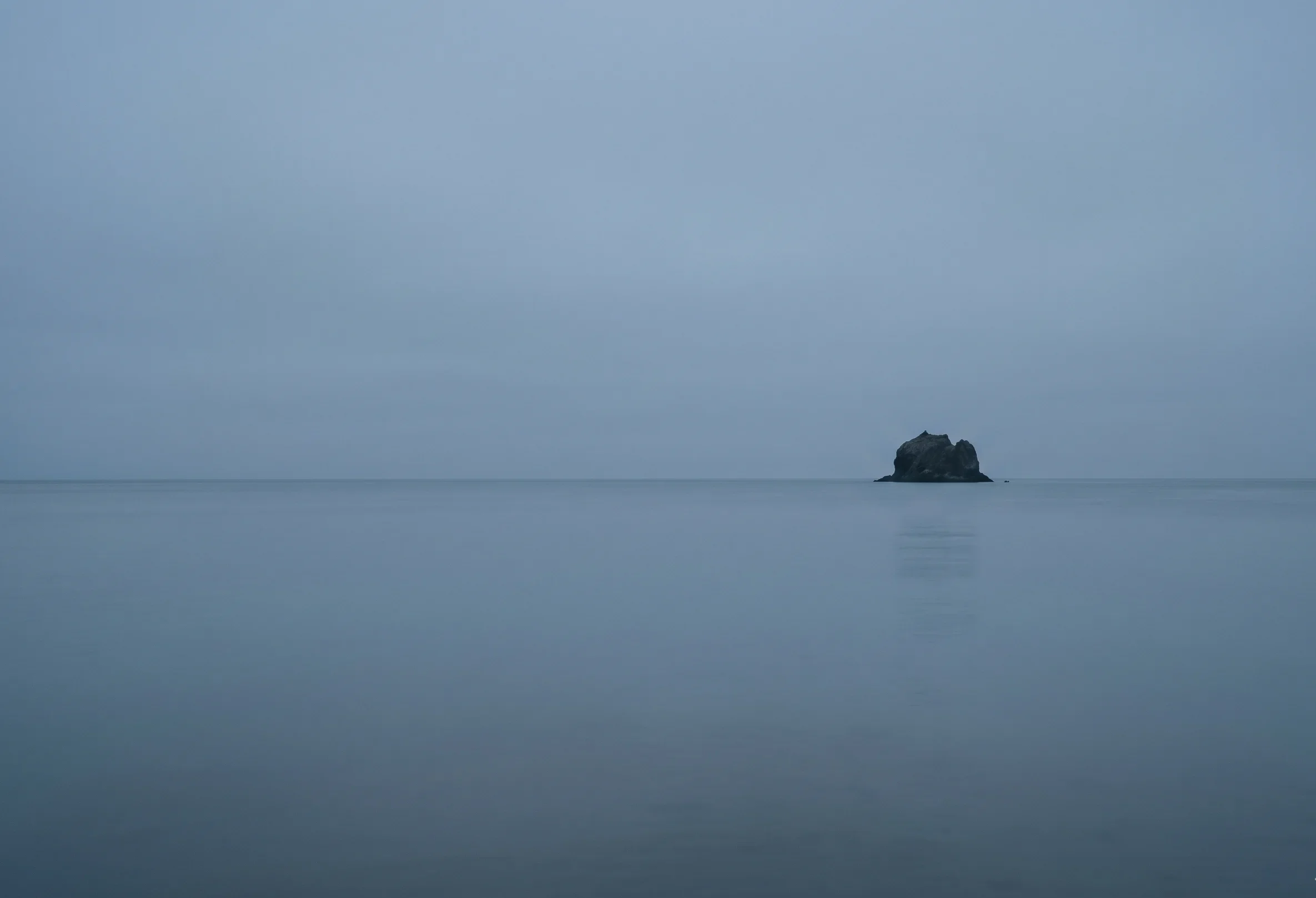 Flat overcast coastal sky meeting still grey-blue water at the horizon, matching the Soft Summer Steel Mist colour #A8B4BE — atmospheric reference for the deepest of the season's blue-grey neutrals.