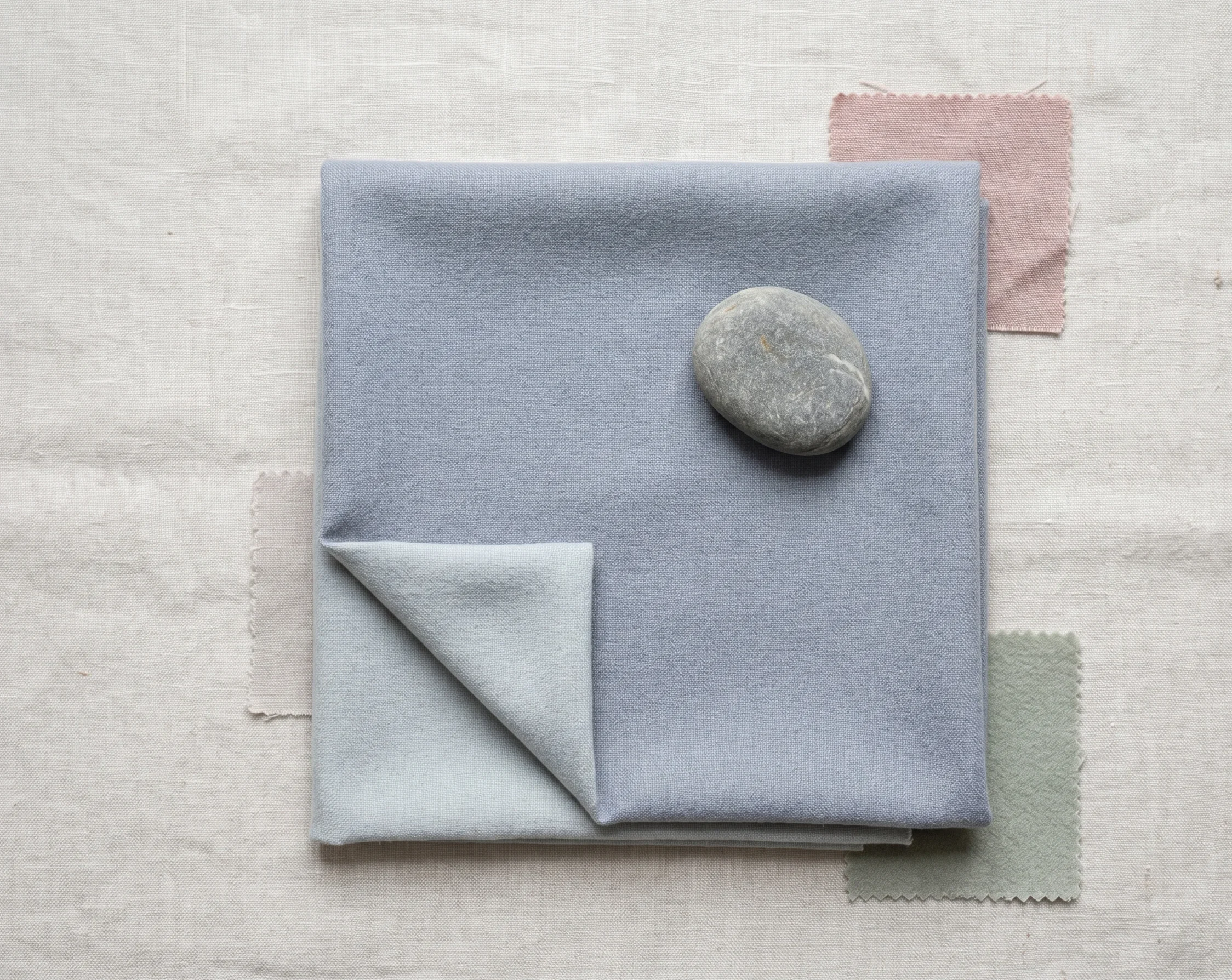 Slate Blue wool fabric square as a capsule wardrobe anchor, layered above a smaller Misty Blue-Grey swatch with dusty rose and sage accents — Soft Summer neutral colour reference.