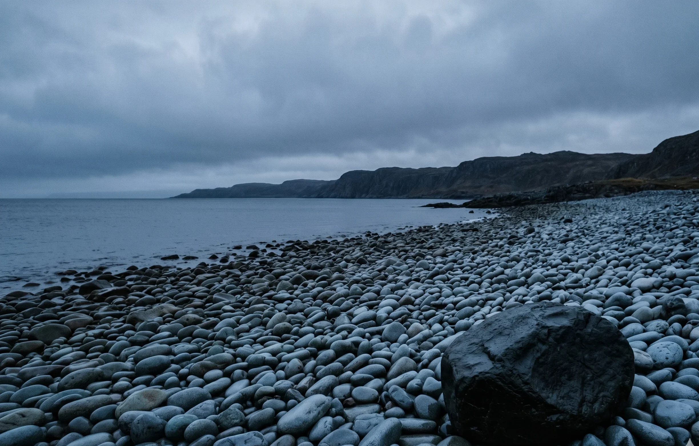 Weathered grey-blue coastal stones on an overcast evening shoreline, matching the Soft Summer Slate Blue colour #B8BEC9 — atmospheric reference for a deep, muted neutral.