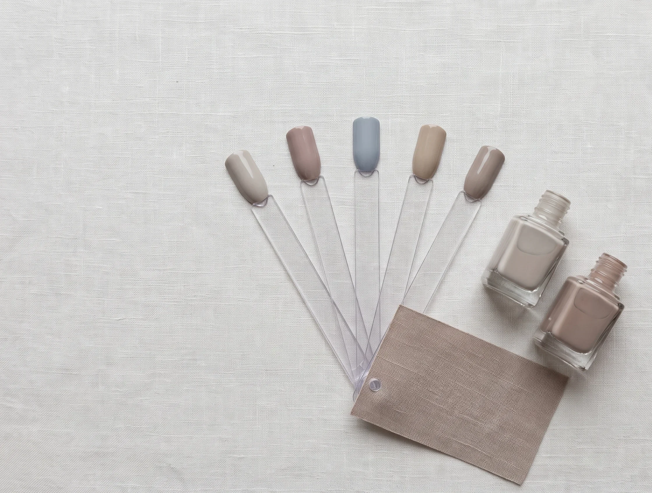 Neutral summer nail colour swatch sticks and polish bottles in cool greige, dusty taupe and soft slate, showing minimalist soft summer nail design options