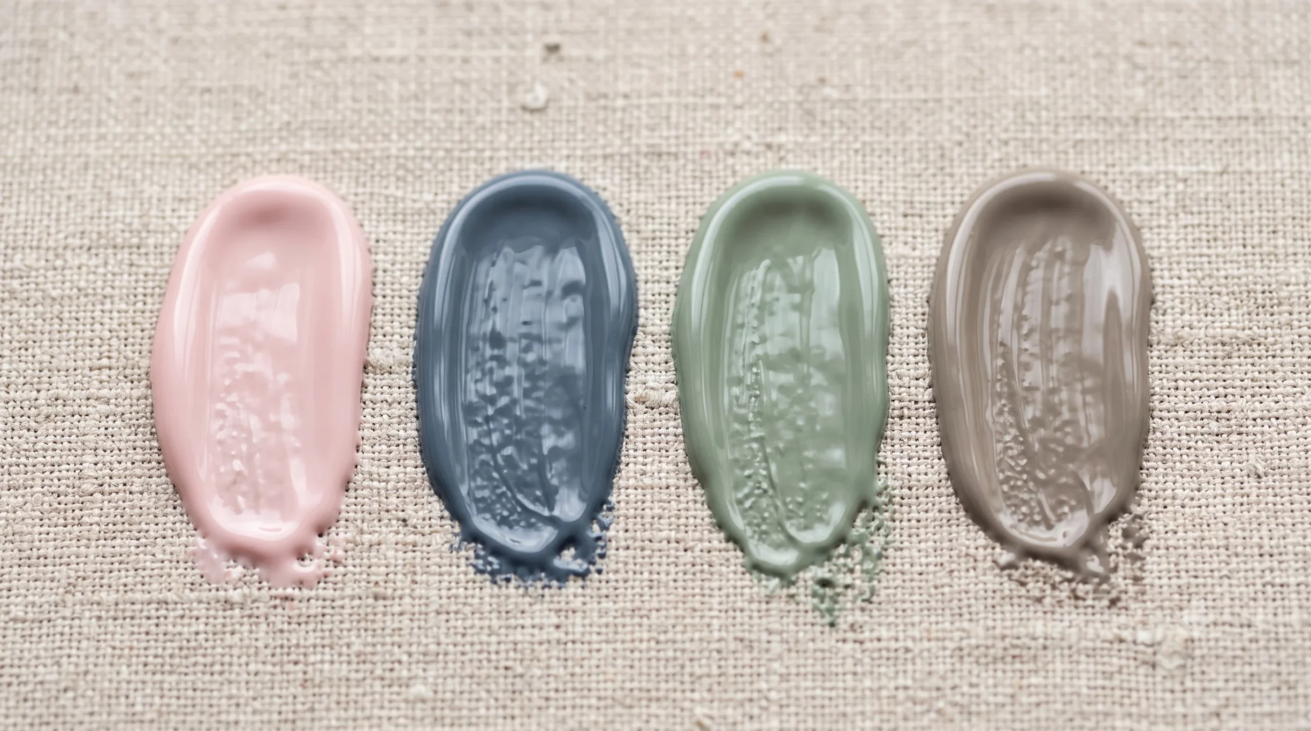 Four thick nail polish smears on linen in soft summer colors: milky pink, slate blue-grey, muted sage, and warm greige.