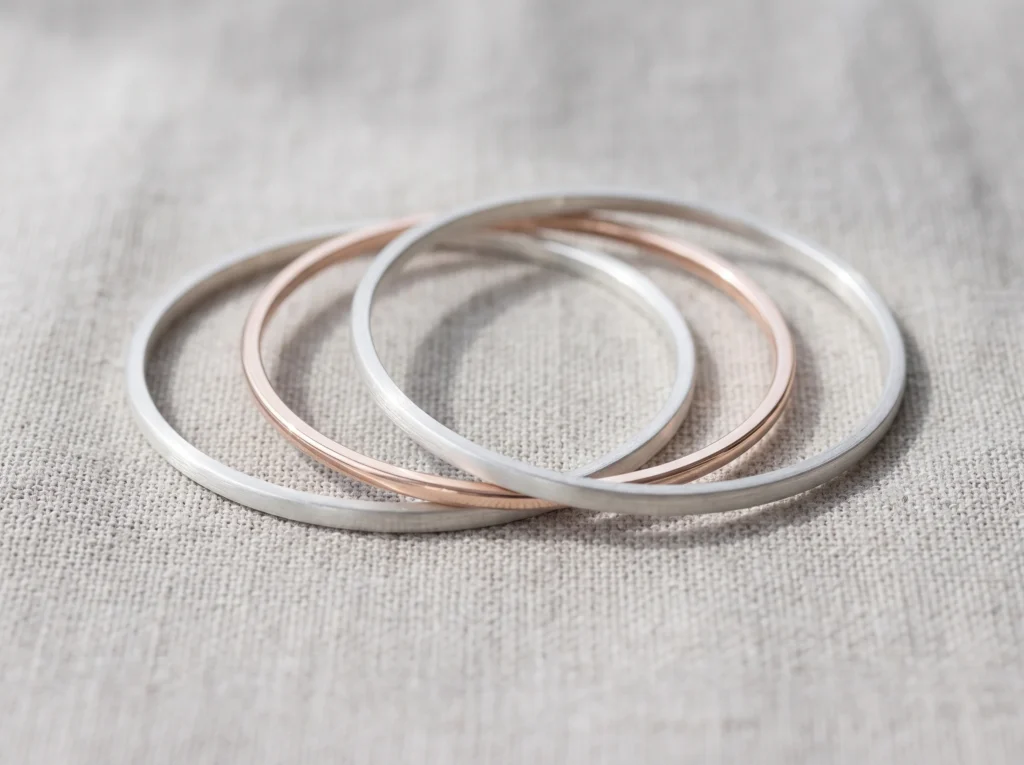Light summer jewelry mixed metal stack with two sterling silver bangles and one pale rose gold bangle

